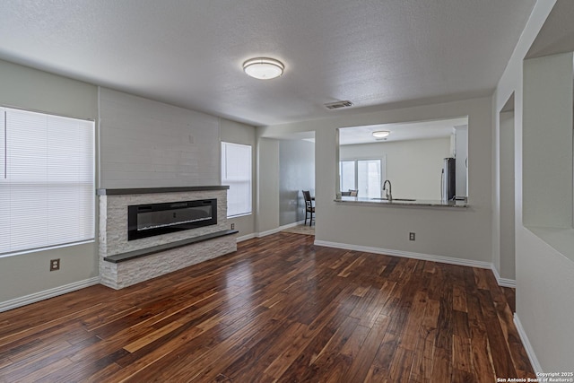 10202 Misty Pln, San Antonio, TX 78245 - unfurnished living room featuring dark wood finished floors, a fireplace, baseboards, a sink, and a textured ceiling