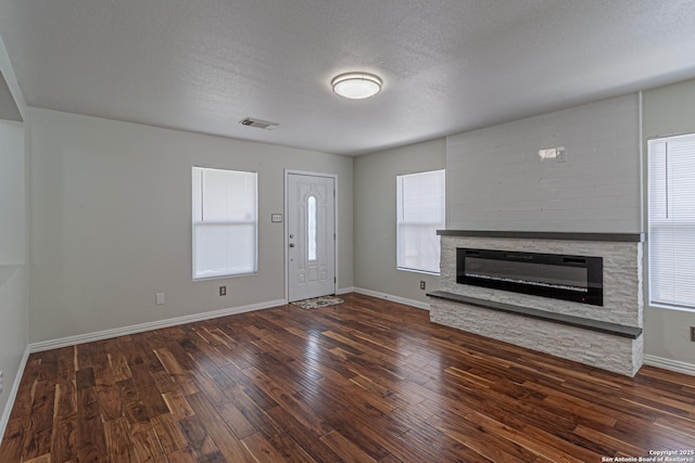 10202 Misty Pln, San Antonio, TX 78245 - unfurnished living room with dark wood-style flooring, a stone fireplace, baseboards, and a textured ceiling
