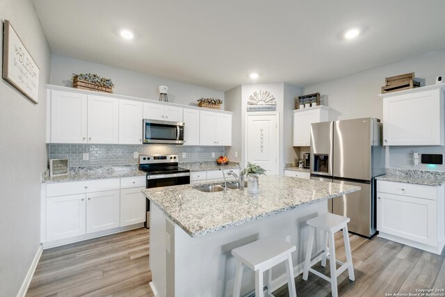 14383 Palm Rdg, San Antonio, TX 78253 - kitchen featuring stainless steel appliances, a sink, light wood finished floors, white cabinets, and decorative backsplash