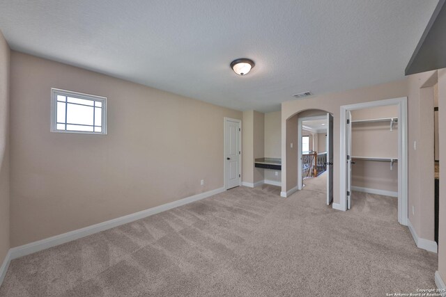 523 White Cyn, San Antonio, TX 78260 - unfurnished bedroom with arched walkways, light colored carpet, baseboards, a textured ceiling, and a walk in closet