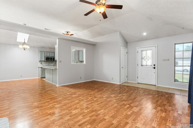 unfurnished living room with light wood finished floors, a ceiling fan, vaulted ceiling, baseboards, and a chandelier