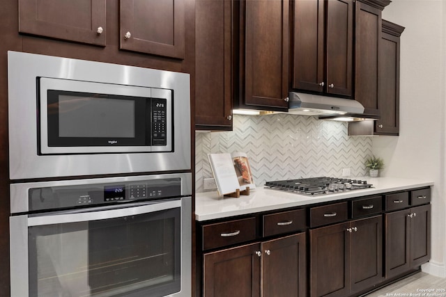 28114 Versant, Boerne, TX 78015 - kitchen with appliances with stainless steel finishes, light countertops, backsplash, under cabinet range hood, and dark brown cabinets
