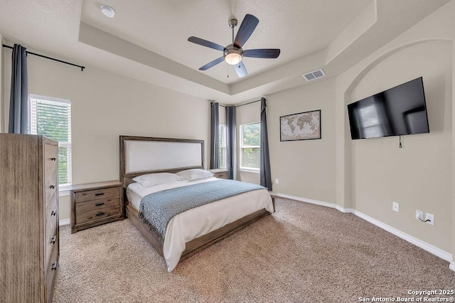 bedroom with a raised ceiling, light carpet, multiple windows, and baseboards