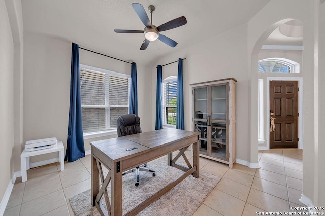 office space featuring light tile patterned floors, baseboards, arched walkways, and a ceiling fan
