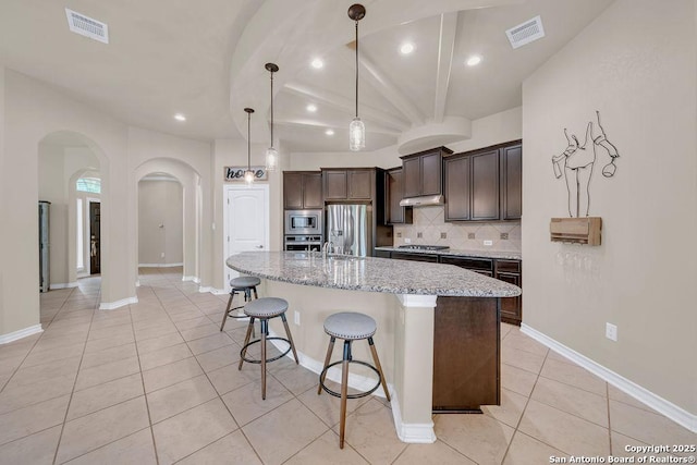 kitchen featuring arched walkways, appliances with stainless steel finishes, dark brown cabinetry, recessed lighting, and tasteful backsplash