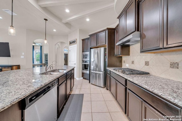 kitchen featuring stainless steel appliances, a sink, under cabinet range hood, tasteful backsplash, and dark brown cabinets