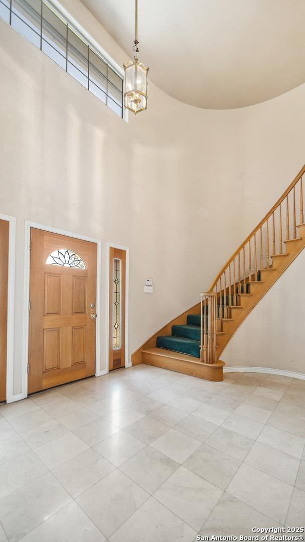 217 Sky View Dr, Adkins, TX 78101 - tiled entrance foyer with stairway, a high ceiling, baseboards, and a chandelier