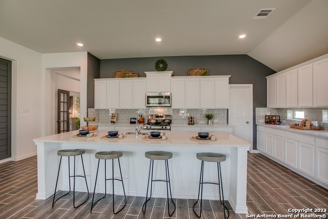 8907 Turkey Crk, Seguin, TX 78155 - kitchen featuring stainless steel microwave, range, dark wood-type flooring, a kitchen bar, and vaulted ceiling