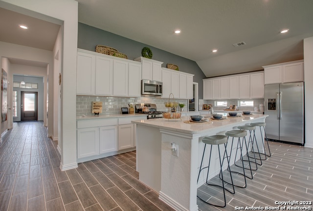 8907 Turkey Crk, Seguin, TX 78155 - kitchen featuring appliances with stainless steel finishes, light wood-type flooring, lofted ceiling, backsplash, and white cabinetry