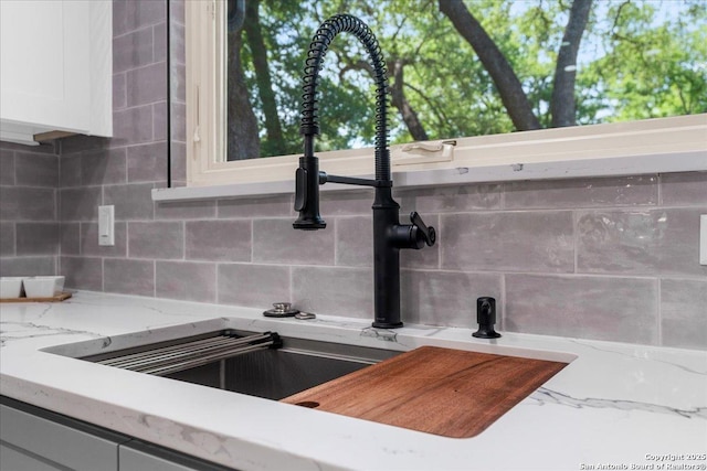 kitchen view of a sink, backsplash, white cabinets, and light stone countertops