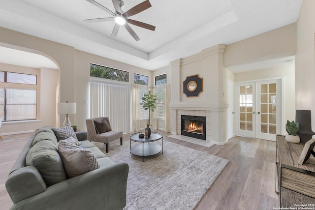 11302 Cedar Park, San Antonio, TX 78249 - living room featuring french doors, ceiling fan, light wood-style flooring, a raised ceiling, and a fireplace