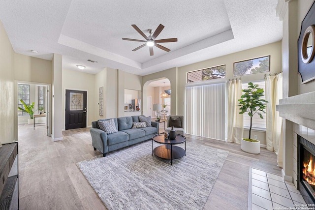 11302 Cedar Park, San Antonio, TX 78249 - living room with a tray ceiling, a textured ceiling, a tiled fireplace, ceiling fan, and arched walkways