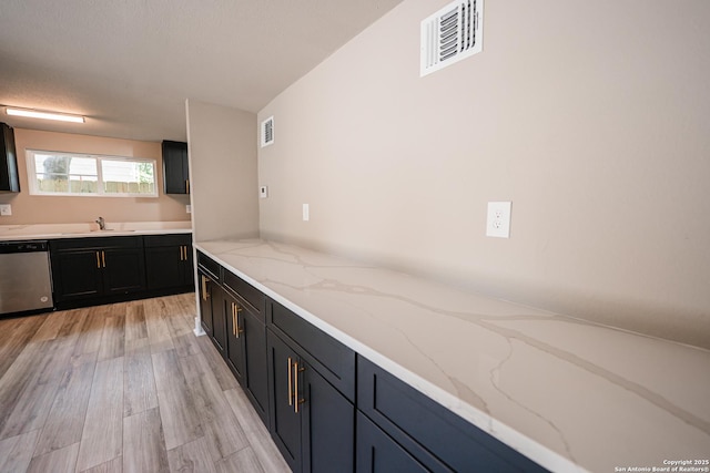 312 Avondale, San Antonio, TX 78223 - kitchen with stainless steel dishwasher, dark cabinetry, light stone countertops, light wood finished floors, and a sink