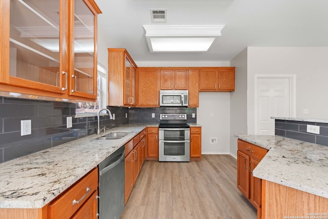 17223 Darlington Run, San Antonio, TX 78247 - kitchen featuring appliances with stainless steel finishes, a sink, brown cabinets, tasteful backsplash, and light wood-style floors