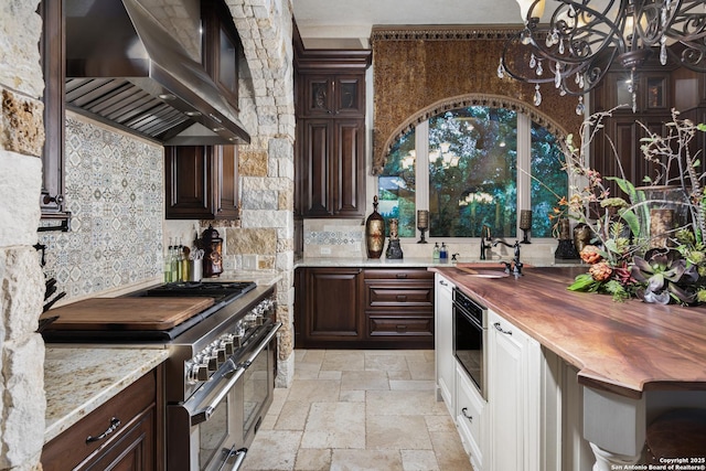 2219 Clubs Dr, Boerne, TX 78006 - kitchen with wall chimney exhaust hood, butcher block counters, range with two ovens, stone tile flooring, and dark brown cabinetry