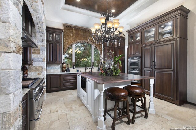 2219 Clubs Dr, Boerne, TX 78006 - kitchen with double oven range, a raised ceiling, stone tile flooring, and a chandelier