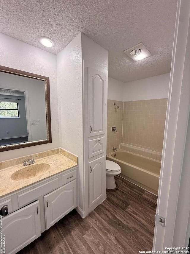 full bathroom with a textured ceiling, wood finished floors, toilet,  shower combination, and vanity
