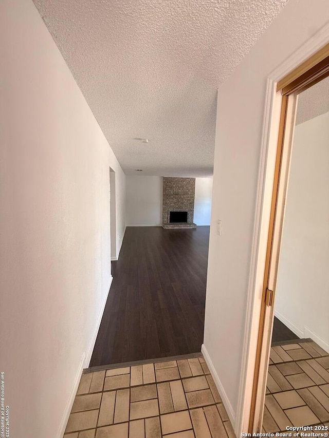 hall with a textured ceiling, baseboards, and light wood-style floors