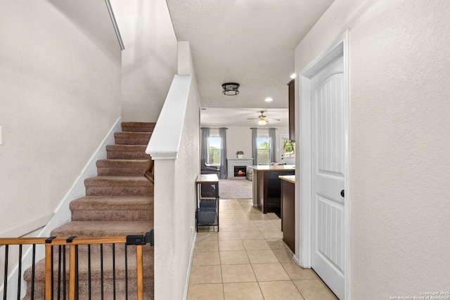160 Jolie, Boerne, TX 78015 - stairs featuring a ceiling fan, a lit fireplace, tile patterned floors, and recessed lighting