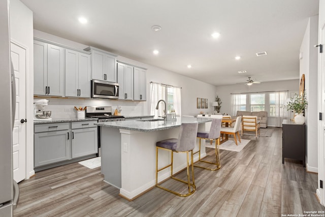 10227 Amaryllis, Boerne, TX 78006 - kitchen featuring appliances with stainless steel finishes, light wood-style flooring, a breakfast bar, an island with sink, and light stone countertops