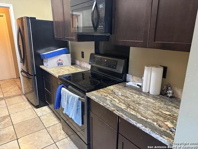 9151 Tree Vlg, San Antonio, TX 78250 - kitchen featuring stainless steel range with electric cooktop, black microwave, light tile patterned flooring, dark brown cabinetry, and light stone counters