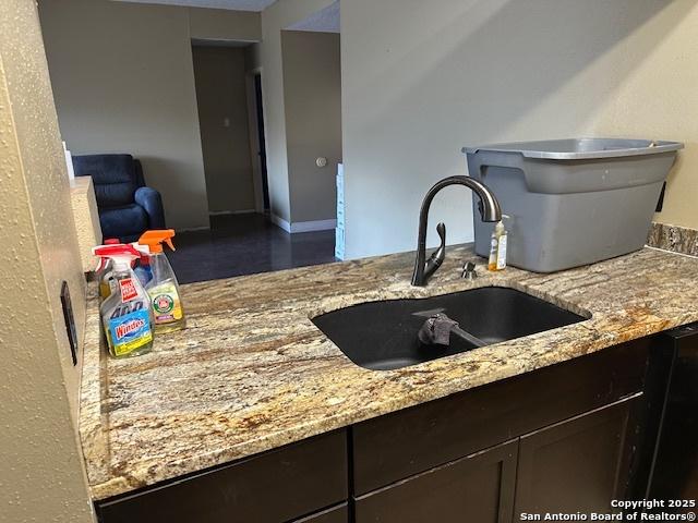 9151 Tree Vlg, San Antonio, TX 78250 - kitchen featuring a sink, light stone countertops, dark brown cabinetry, and baseboards