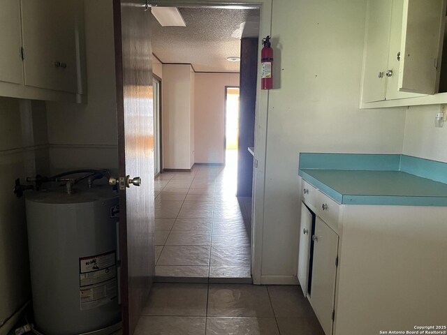 608 Leona St, Cotulla, TX 78014 - kitchen with water heater, light tile patterned flooring, a textured ceiling, and white cabinets