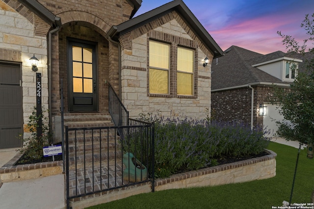 entrance to property with stone siding, brick siding, fence, a gate, and an attached garage