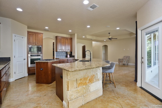 12302 Calvert, Helotes, TX 78023 - kitchen with arched walkways, stainless steel appliances, an island with sink, decorative backsplash, and a sink