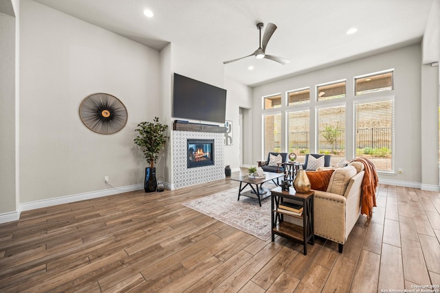 living room with wood finished floors, a ceiling fan, a tile fireplace, recessed lighting, and baseboards
