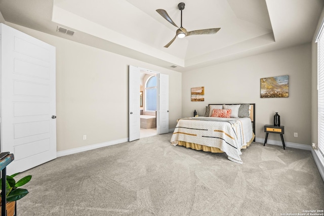 bedroom featuring a raised ceiling, carpet floors, baseboards, and ensuite bathroom