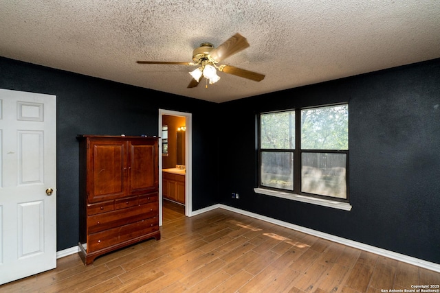 8013 County Road 128, Floresville, TX 78114 - unfurnished bedroom featuring light wood-style floors, a textured ceiling, baseboards, ceiling fan, and ensuite bathroom