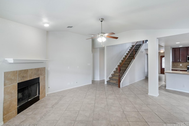 7326 Concerto Dr, San Antonio, TX 78266 - unfurnished living room with vaulted ceiling, a ceiling fan, stairway, a tiled fireplace, and light tile patterned flooring