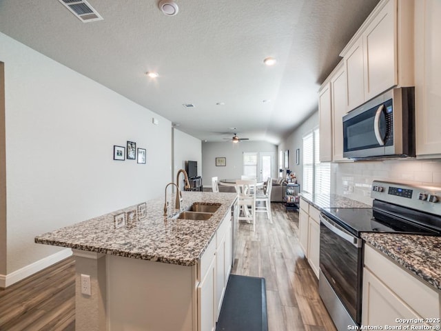 3075 Mondavi Crst, Schertz, TX 78154 - kitchen with appliances with stainless steel finishes, a sink, light wood-style flooring, an island with sink, and decorative backsplash