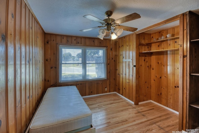 255 Gilbert Ln, San Antonio, TX 78213 - unfurnished bedroom featuring wooden walls, baseboards, light wood-style flooring, a textured ceiling, and ceiling fan