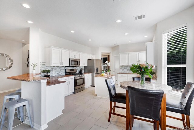 20607 Wild Spgs, San Antonio, TX 78258 - kitchen featuring appliances with stainless steel finishes, a peninsula, a kitchen bar, backsplash, and white cabinets