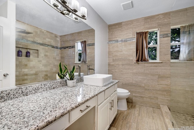 20607 Wild Spgs, San Antonio, TX 78258 - bathroom featuring tile walls, vanity, toilet, and tiled shower