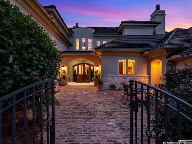 52 Oakland Hls, Boerne, TX 78006 - exterior entry at dusk with stucco siding, french doors, a chimney, stone siding, and a standing seam roof
