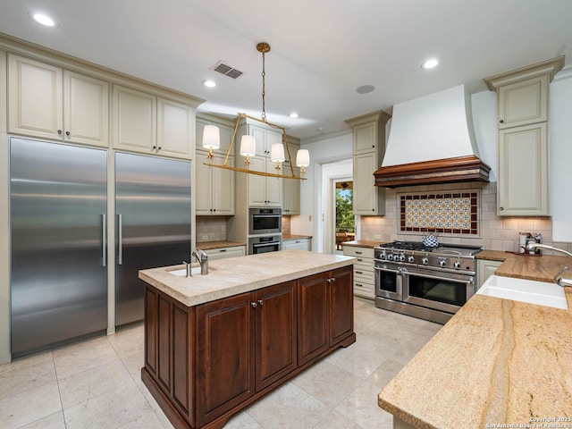 52 Oakland Hls, Boerne, TX 78006 - kitchen featuring high quality appliances, cream cabinets, premium range hood, a sink, and a kitchen island with sink