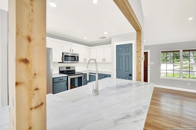 661 Abels Way, Canyon Lake, TX 78133 - kitchen featuring appliances with stainless steel finishes, backsplash, white cabinets, baseboards, and light wood-style flooring