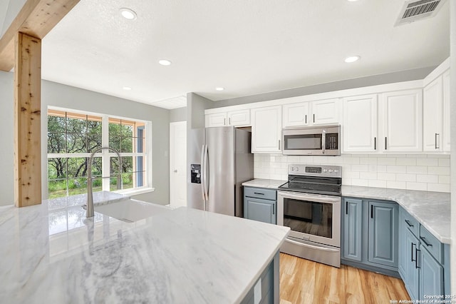 661 Abels Way, Canyon Lake, TX 78133 - kitchen with stainless steel appliances, decorative backsplash, white cabinetry, light wood-style floors, and light stone countertops