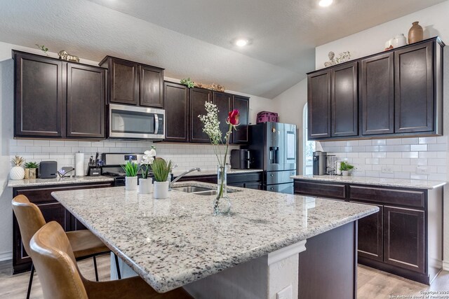 9614 Tupelo Holw, San Antonio, TX 78254 - kitchen featuring appliances with stainless steel finishes, a sink, a kitchen breakfast bar, vaulted ceiling, and dark brown cabinets