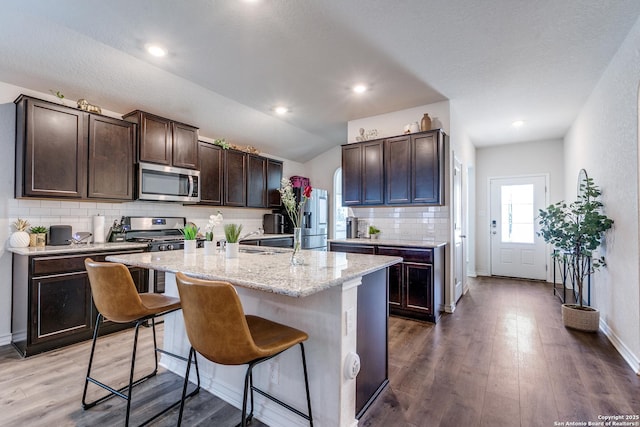 9614 Tupelo Holw, San Antonio, TX 78254 - kitchen featuring appliances with stainless steel finishes, dark brown cabinets, a breakfast bar, decorative backsplash, and wood finished floors