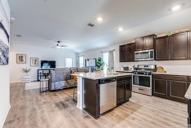 9614 Tupelo Holw, San Antonio, TX 78254 - kitchen featuring appliances with stainless steel finishes, a center island with sink, dark brown cabinetry, light wood finished floors, and lofted ceiling