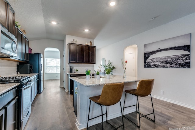 9614 Tupelo Holw, San Antonio, TX 78254 - kitchen with arched walkways, appliances with stainless steel finishes, dark wood-style floors, a breakfast bar, and lofted ceiling