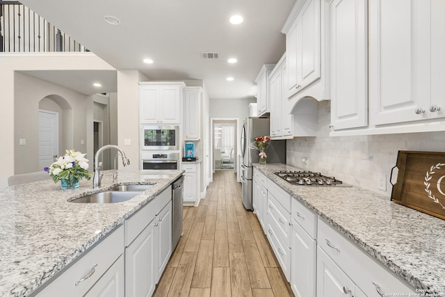 8823 Hideout, San Antonio, TX 78254 - kitchen featuring a sink, appliances with stainless steel finishes, light wood finished floors, white cabinets, and backsplash