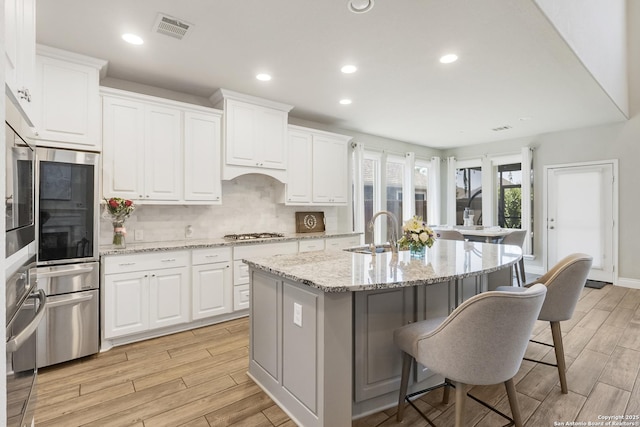8823 Hideout, San Antonio, TX 78254 - kitchen featuring a sink, a kitchen breakfast bar, an island with sink, light wood-style floors, and white cabinetry