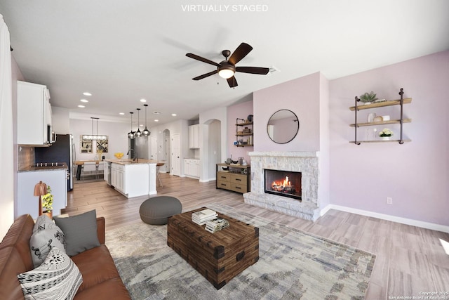 2060 Oedipus, San Antonio, TX 78245 - living room featuring light wood-style flooring, arched walkways, a stone fireplace, ceiling fan, and baseboards
