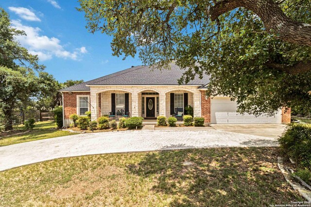 573 Mountain Oaks Dr, Canyon Lake, TX 78133 - view of front facade with covered porch, driveway, an attached garage, brick siding, and roof with shingles