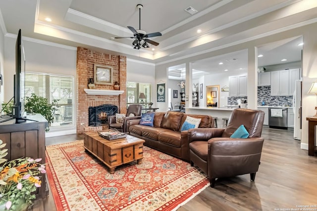573 Mountain Oaks Dr, Canyon Lake, TX 78133 - living room with a ceiling fan, a brick fireplace, light wood finished floors, ornamental molding, and a raised ceiling